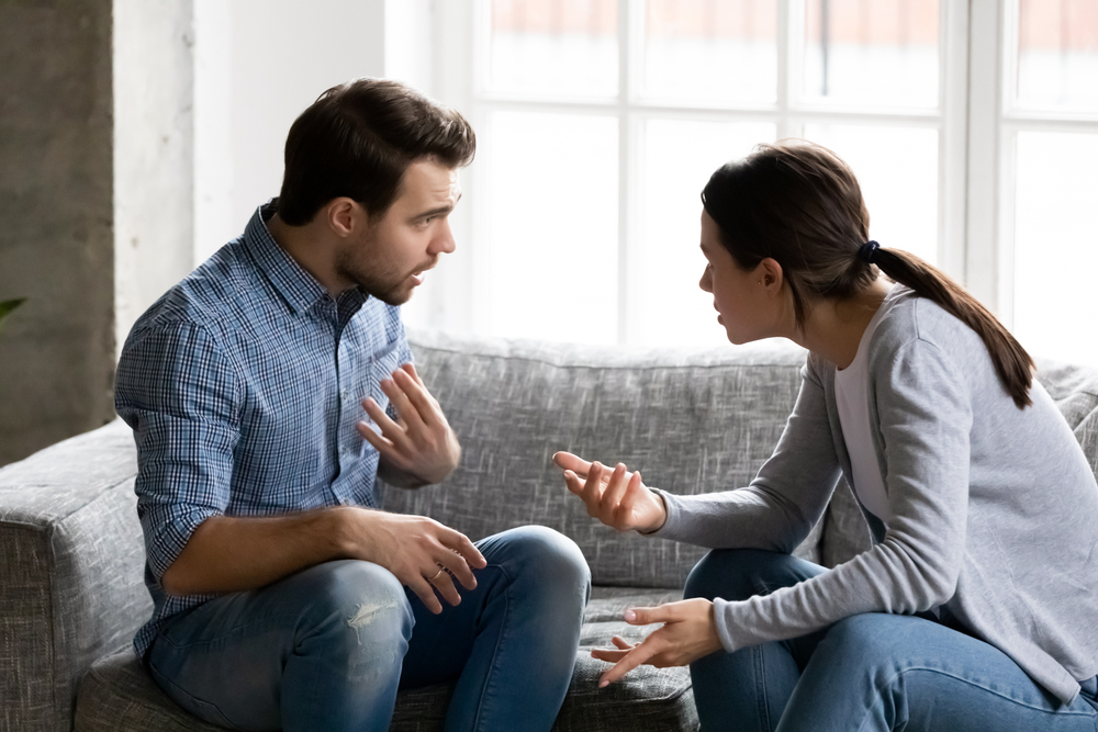 stressed young married family couple arguing emotionally, blaming lecturing each other, sitting on couch