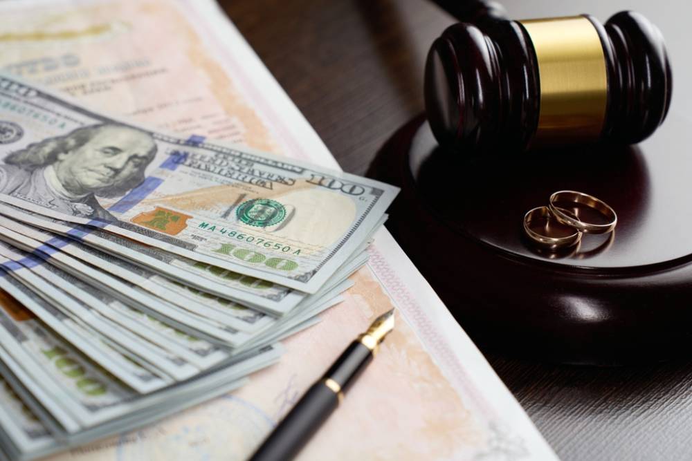 Legal Separation and Alimony Concept. Wedding rings, judge gavel, US dollar bills and blurred marriage certificate