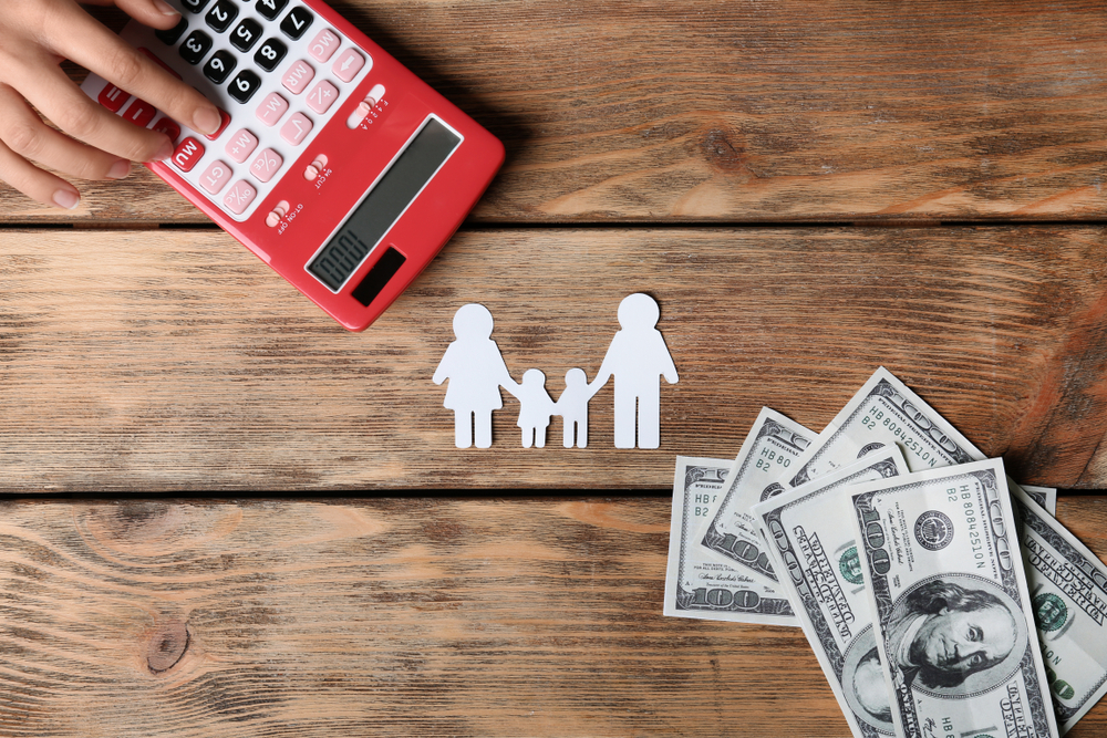 Woman using calculator and paper silhouette of family on wooden background